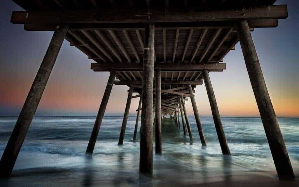 Under the pier at Emerald Isle at sunset as waves crash on the shore