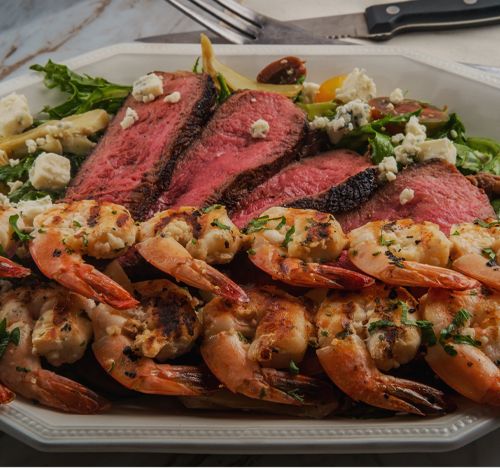 Slices of rare grilled steak and charred shrimp over a green salad with blue cheese." title="Explore local dining near Crystal Coast rentals