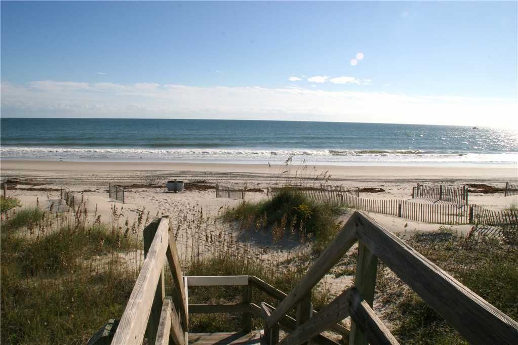 A view from wooden stairs leading down to a wide, sandy beach and the sparkling Atlantic Ocean, showcasing the convenient private beach access available to guests staying at a Spectrum Properties vacation rental in Emerald Isle.