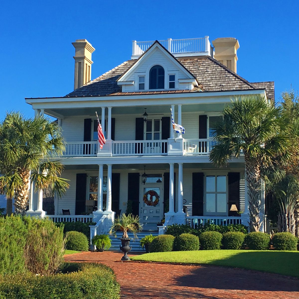 A stunning white historic home in Beaufort, North Carolina, featuring classic double-decker porches, a widow's watch, and manicured landscaping with palm trees, representing the timeless coastal charm found near Spectrum Properties vacation rentals.